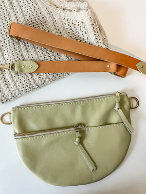 Green leather handbag with a brown strap on a styled background